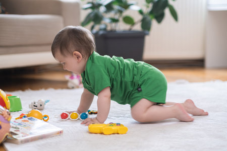Curious baby boy crawling on white fluffy rug near scattered toys and books adorable chubby kid in green outfit enjoying exploring new things in living room at homeの写真素材
