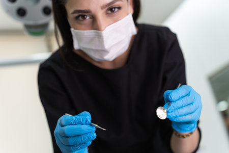Positive dentist wearing disposable mask holding metal instruments to examine patient teeth at appointment in stomatology center doctor with test tools for oral cavityの写真素材
