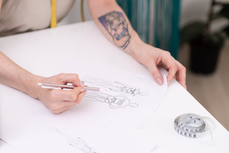 Lady designer draws clothes model on paper at table in fashion atelier tailor makes pencil sketch of apparel for women in sewing studio closeup dressmaking industryの写真素材