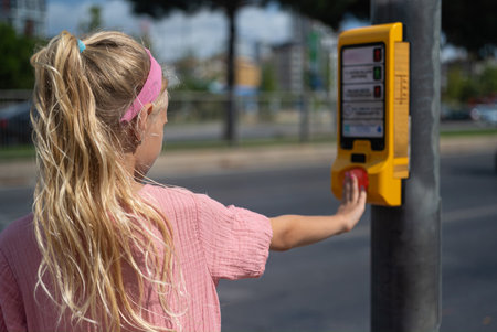 A girl child confidently presses the pedestrian crossing button, activating the green light on the...