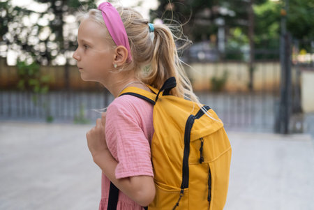 Schoolgirl, pink dress, with a sunny yellow backpack, near the elementary school.