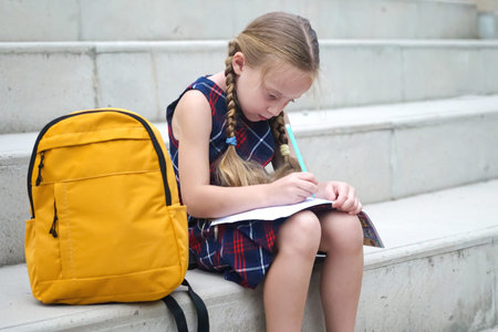 A happy schoolgirl, her yellow backpack close at hand, diligently completes her outdoor homework...