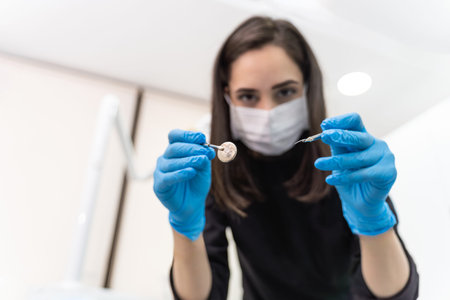 Young female dentist with mask and gloves holding sterile instruments for examining patient at...