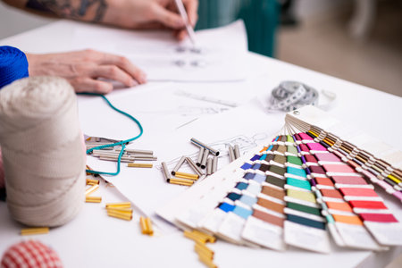 Color swatch palette and small metal tubes on tailor desk in sewing atelier dressmaker draws outfit model sketch in craft dressmaking workshop closeupの写真素材