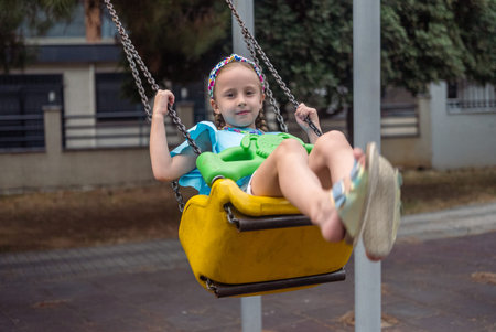 Smiling child enjoys the swings at the city park playground.の写真素材