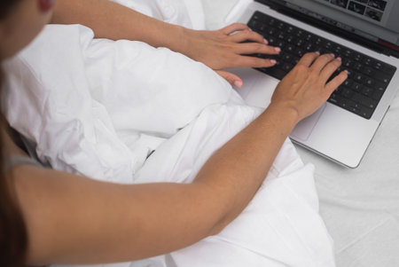 Woman communicates online in social networks sitting in bed at home female hands lie on white...