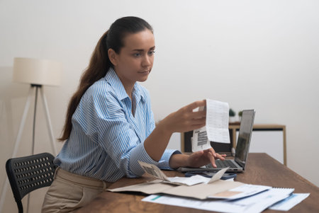 An engaged woman at home, handling bills on her laptop. Calculating taxes, scrutinizing bank...