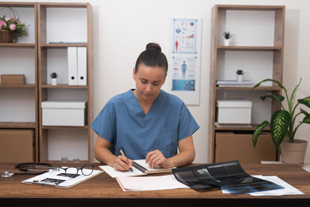Doctor makes notes in notebook sitting at desk with pictures of X-rays examination female therapist...