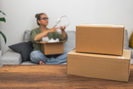 Mock-up parcel boxes on a table, with a woman in the background unboxing an online shopping delivery, illustrating the essence of shipping and marketplace shopping.の写真素材
