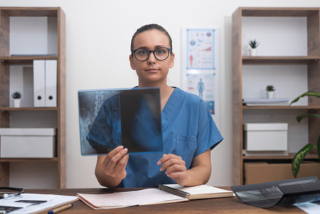 Doctor shows X-ray picture looking at camera sitting in office female in blue lab coat films lesson to students explaining results of patient examination online educationの写真素材
