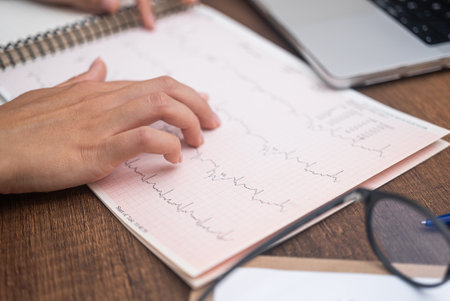 Female hand touches cardiogram on table closeup cardiologist works with results of patient examination sitting in office professional medical care in modern hospitalの写真素材