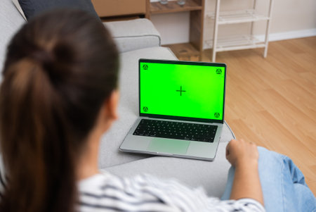 Woman works on computer sitting on sofa closeup female freelancer works at home looking at screen with chromakey backside view modern technologies of remote communicationの写真素材