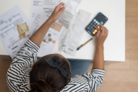 Focused woman counts utility bank bills with calculator of smartphone sitting at desk with documents female works in office of accommodation upper viewの写真素材