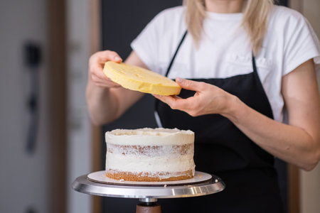 Professional confectioner in black apron connecting gluten free cake layers smeared with white cream...