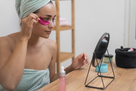 Beauty ritual: A woman, at the mirror, applies pink under-eye patches, elevating her skincare with professional cosmetics.の写真素材