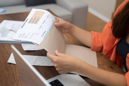 Lady takes out papers from envelope containing utility bills woman examines bank payments with monthly amount sitting at workplace with open laptop at homeの写真素材