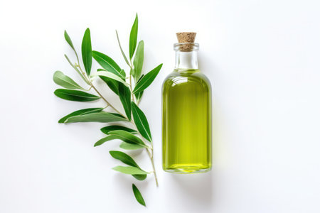 A clear glass bottle of olive oil accompanied by fresh green olive branches on a white background.の素材
