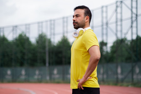 Confident man looking into distance and holding hands in waist at training at city sports stadium professional sportsman enjoying jogging on modern trackの写真素材