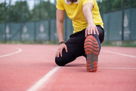 Energetic athlete in activewear and headphones warms up on the red running track at a city sports ground.の写真素材