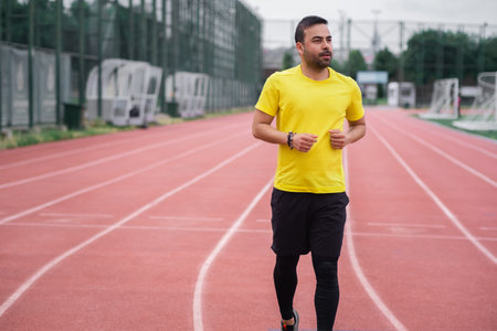 Energetic young man jogging along an empty track with a red rubber surface and crisp white markings...