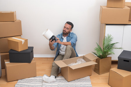 In the midst of relocation, a young man unboxing a lamp from among unpacked boxes in his new apartment, determined to make it homeの写真素材