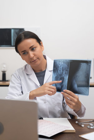 Virtual Consultation: A doctor, through online medicine and telehealth, points at an X-ray film on a laptop during a video chat in the clinic.の写真素材