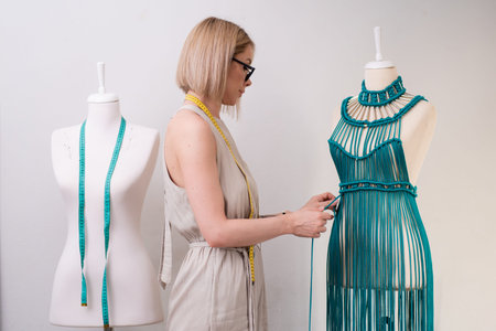 Designer creates unique green macrame dress on dummy in sewing atelier blonde woman ties knot on...