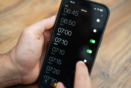 Male person hand selects appropriate time activating alarm clock on modern smartphone to wake up...