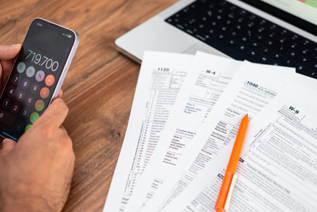 Man hand holds smartphone making financial calculations to report annual income by filling tax forms...