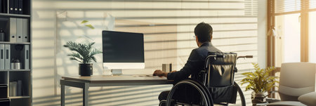 Man in a wheelchair working at a desk in a brightly lit office. Workplace accessibility and employment for disabled individuals.の素材