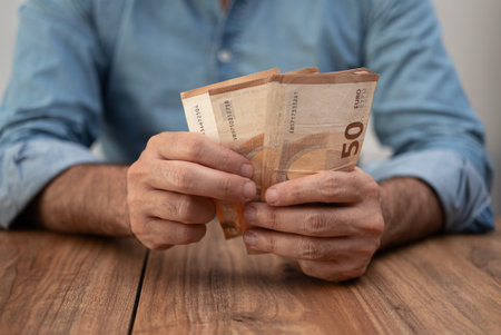 Man entrepreneur holds euro banknotes counting money with attention preparing cash for paying salary to workers in end of work shift sitting at workplace in officeの写真素材