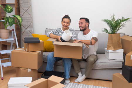 Positive newlyweds celebrate purchase of new apartment together sitting on soft sofa among...