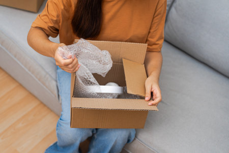 On her sofa, a cheerful lady unboxes a parcel, revealing new headphones, relishing her successful online shopping adventure.の写真素材