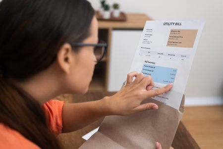 Budget Insight: With an envelope in hand, a woman closely inspects a utility bill, vividly exposing taxes and household costsの写真素材