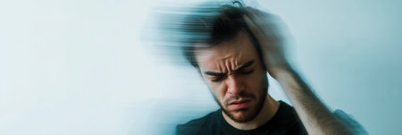 Young man is experiencing dizziness and imbalance, touching his head with a pained expression. The blurred background evokes the sensation of disorientationの素材