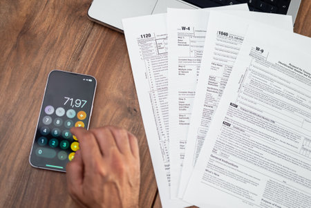 Close-up of a person calculating taxes on a smartphone with tax forms spread out on a wooden desk. Tax preparation. Perfect for accounting, tax season, and financial managementの写真素材