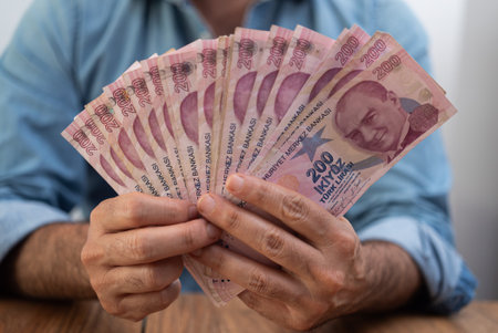 Person displaying fanned out Turkish lira banknotes on a wooden table. Represents financial transactions, economic instability, and currency valueの写真素材