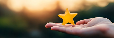 Hand holding a small golden five pointed star against a blurred sunset background, symbolizing customer satisfaction and excellence in hospitality and service industriesの素材