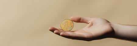 Male hand demonstrating golden bitcoin on neutral background, representing investment, finance, and digital currency in modern business worldの素材