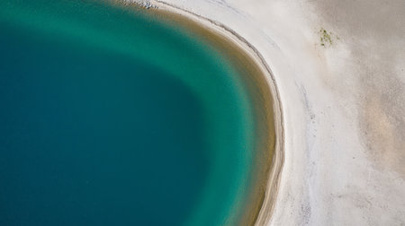 Artificial lake with turquoise water meets a white sandy shore, creating a striking contrast in an aerial view, highlighting environmental themes of sustainability and eco consciousnessの素材