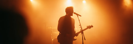 Silhouette of a male singer and guitarist performing passionately on stage, illuminated by vibrant orange lights, creating an energetic atmosphere filled with music and emotionの素材