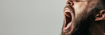 Close up of a bearded man screaming with his mouth wide open, expressing intense emotion against a neutral background, conveying concepts of anger, frustration, or protestの素材