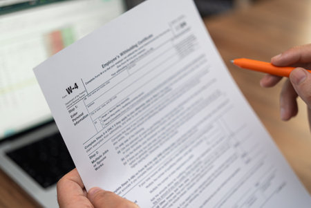 Newly hired employee compares data in modern laptop to fill W-4 form to determine federal tax withholding for new job sitting at desk in office with penの写真素材