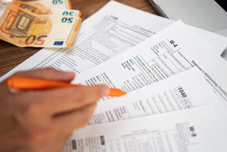 Male freelancer hand holds pen preparing for filling tax forms keeping detailed records of income and expenses sitting at workplace with euro banknotesの写真素材