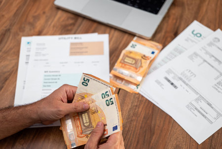 Mature man hands with euros bills fan over printed utility bills on office table closeup, middle...