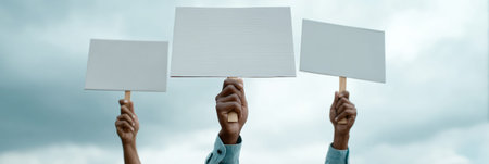 Activists holding blank protest signs during an immigration rights demonstration, advocating for policy change and social justice under a cloudy skyの素材