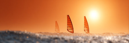 Windsurfers skillfully navigating ocean waves at sunset, with the sky awash in vibrant orange and gold hues, create a stunning scene of athleticism and natural beautyの素材