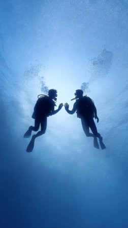 Two scuba divers are giving a high five underwater, creating a silhouette against the bright blue water, bubbles rising around them as they enjoy their diveの素材