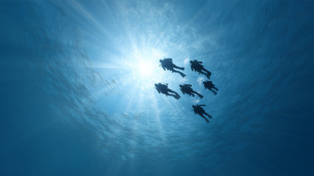 Sunbeams filtering through the surface illuminate a group of scuba divers as they explore the vibrant depths of the blue ocean, creating a captivating underwater spectacleの素材
