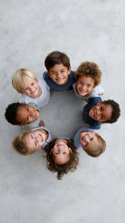 From a high angle perspective, a diverse group of smiling children forms a circle on a gray concrete surface, symbolizing unity, friendship, and the joy of childhoodの素材